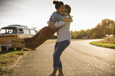 Happy couple doing a road trip with a camper, embracing on the road - UUF16200