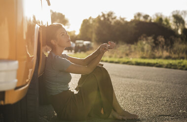 Pretty woman on a road trip with her camper, relaxing at the roadside - UUF16214