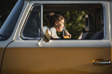 Pretty woman on a road trip with her camper, taking a break, drinking juice - UUF16217