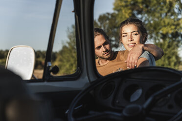 Affectionate couple standing by their camper with arms around - UUF16218