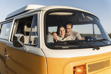 Affectionate couple sitting in their camper with arms around, watching sunset - UUF16220
