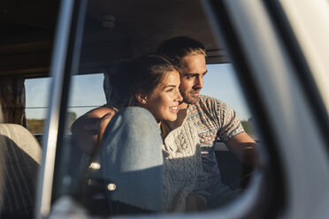 Affectionate couple sitting in their camper with arms around, watching sunset - UUF16222