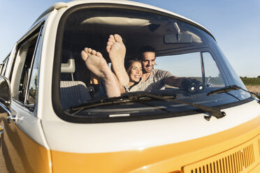 Happy couple sitting in their camper with bare feet up - UUF16223