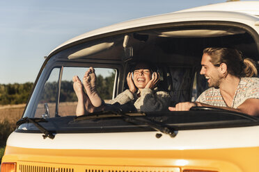 Happy couple sitting in their camper with bare feet up, listening music - UUF16229