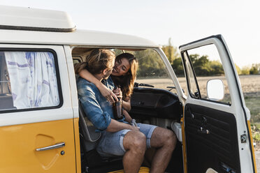 Happy couple sitting in their camper, embracing, drinking beverage - UUF16245