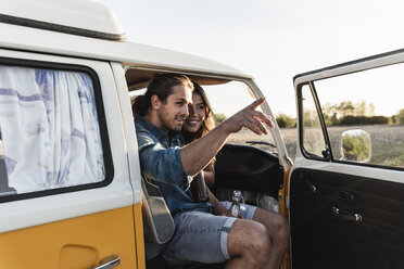 Ein glückliches Paar sitzt in seinem Wohnwagen, der Mann zeigt in die Ferne - UUF16246