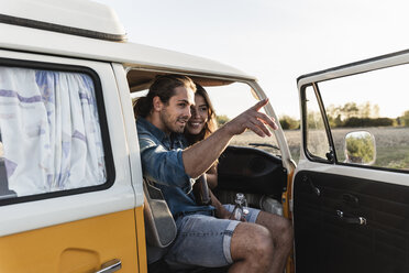 Happy couple sitting in their camper, man pointing at distance - UUF16246