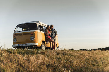 Young couple leaning on their camper watching the sunset - UUF16254