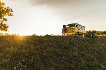 Young couple leaning on their camper watching the sunset - UUF16256