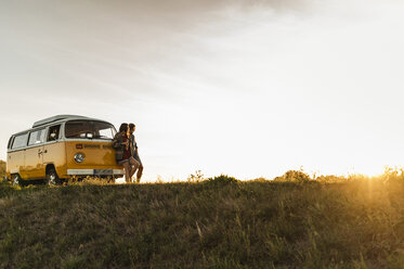 Young couple leaning on their camper watching the sunset - UUF16257