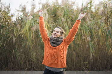 Porträt einer lächelnden Frau mit orangefarbenem Strickpullover und Schal im Herbst - MOEF01831