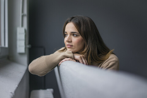 Porträt einer Frau, die sich auf der Couch entspannt und aus dem Fenster schaut, lizenzfreies Stockfoto