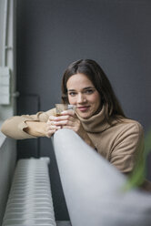 Porträt einer lächelnden Frau, die sich auf der Couch mit einem Glas Kaffee entspannt - MOEF01835