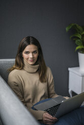 Portrait of content woman wearing light brown turtleneck pullover sitting on couch with laptop - MOEF01839