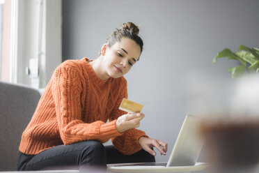 Portrait of content woman sitting on couch using laptop and credit card - MOEF01847