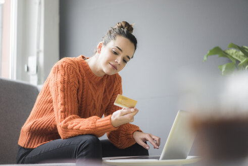 Porträt einer zufriedenen Frau, die mit Laptop und Kreditkarte auf der Couch sitzt - MOEF01847