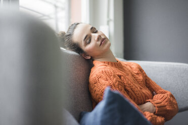 Porträt einer Frau mit orangefarbenem Strickpullover, die sich auf der Couch ausruht - MOEF01848