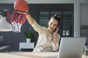 Porträt eines Freiberuflers am Telefon, der am Arbeitsplatz einen Basketball in einen Korb wirft - MOEF01856