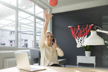 Freiberufler am Telefon, der einen Basketball in einen Korb auf einem Dachboden wirft - MOEF01857