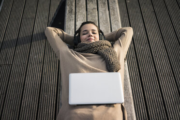 Portrait of smiling woman lying on bench listening music with cordless headphones - MOEF01866