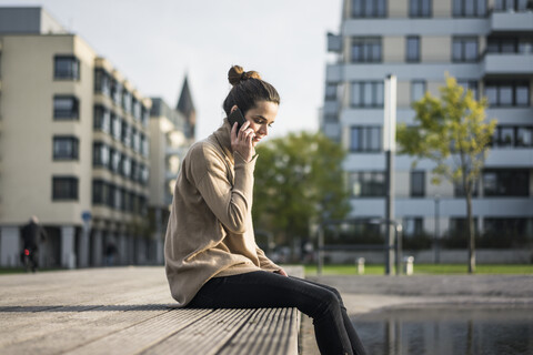 Frau am Telefon sitzend auf Bank im Herbst, lizenzfreies Stockfoto