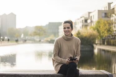 Portrait of smiling woman with digital tablet sitting on bench in autumn - MOEF01870