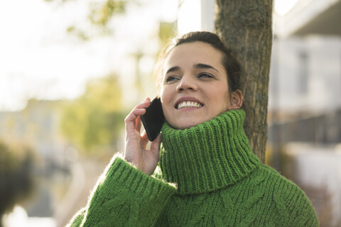 Porträt einer glücklichen Frau am Telefon mit grünem Rollkragenpullover im Herbst, lizenzfreies Stockfoto