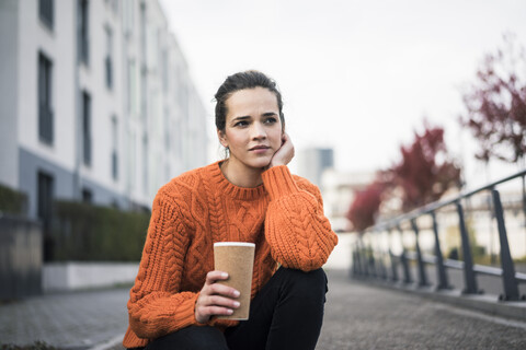 Portrait of pensive woman with coffee to go wearing orange knit pullover outdoors stock photo