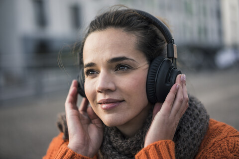 Porträt einer lächelnden Frau, die mit schnurlosen Kopfhörern im Herbst Musik hört, lizenzfreies Stockfoto