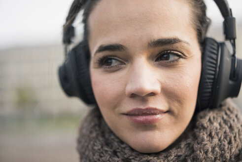 Porträt einer lächelnden Frau mit Schal, die mit schnurlosen Kopfhörern Musik hört, Nahaufnahme - MOEF01882
