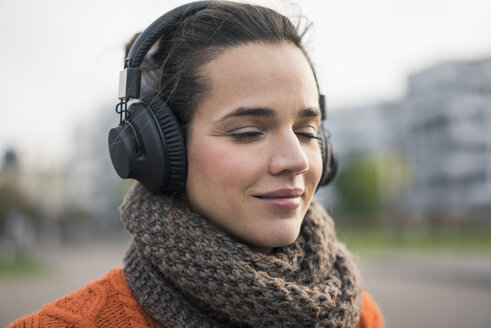 Porträt einer lächelnden Frau mit Schal, die mit schnurlosen Kopfhörern Musik hört - MOEF01883