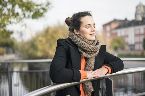 Porträt einer Frau im Herbst, die sich entspannt an ein Geländer lehnt, lizenzfreies Stockfoto