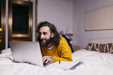 Lächelnder junger Mann, der zu Hause im Bett liegt und einen Laptop benutzt - JRFF02154