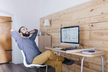 Smiling young man sitting at desk with floor plan on the computer - JRFF02163