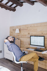 Smiling young man sitting at desk with floor plan on the computer - JRFF02164