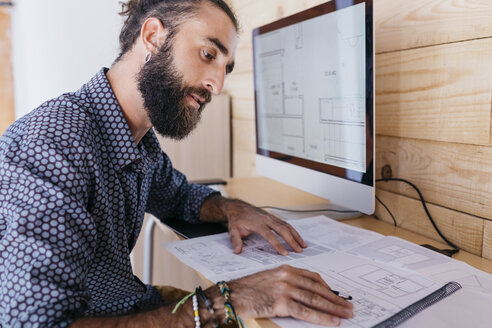 Young architect working at home with blueprints and computer - JRFF02167