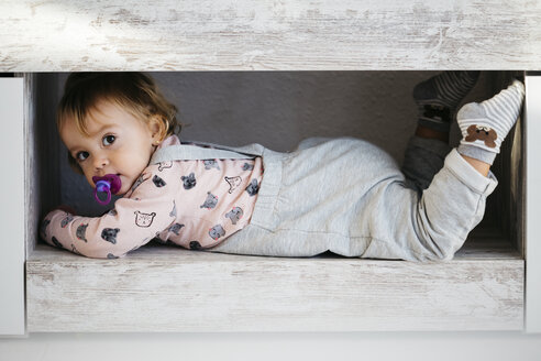 Porträt eines kleinen Mädchens mit Schnuller, das sich zu Hause versteckt - JRFF02183