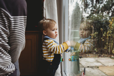 Niedlicher Sohn schaut durch das Fenster der Mutter zu Hause - CAVF57966