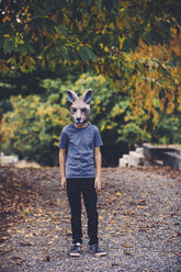 Junge in voller Länge, der eine Tiermaske trägt, während er zu Halloween bei den Bäumen steht - CAVF57974