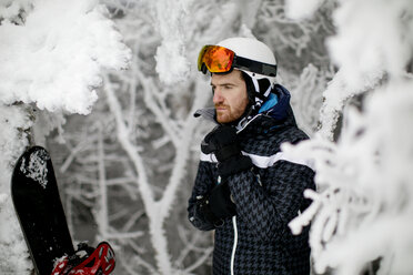 Selbstbewusster Mann mit Skihelm inmitten gefrorener Bäume im Winter - CAVF57996