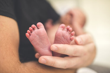 Midsection of father carrying newborn daughter while sitting at home - CAVF58008