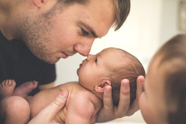 Vater, der seine neugeborene Tochter trägt, während er bei seinem Sohn zu Hause sitzt - CAVF58009