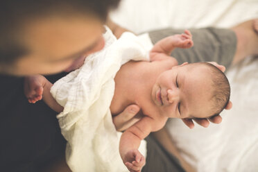 Hoher Blickwinkel des Vaters, der seine schlafende neugeborene Tochter trägt, während er zu Hause auf dem Bett sitzt - CAVF58010