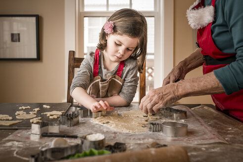 Enkelin hilft Großmutter beim Backen von Weihnachtsplätzchen auf dem Tisch zu Hause - CAVF58019