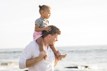 Father carrying daughter on shoulders while standing at beach against clear sky - CAVF58025