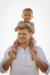 Porträt eines Vaters, der seine Tochter auf den Schultern trägt, während er am Strand vor einem klaren Himmel steht - CAVF58026