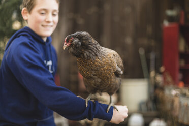 Nahaufnahme eines Jungen, der mit einem Huhn auf einer Geflügelfarm spielt - CAVF58075