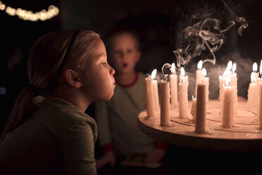 Schwester bläst Kerzen auf dem Tisch während Weihnachten mit Bruder im Hintergrund zu Hause - CAVF58079