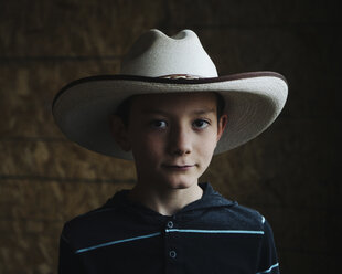 Close-up portrait of confident boy wearing cowboy hat at barn - CAVF58095