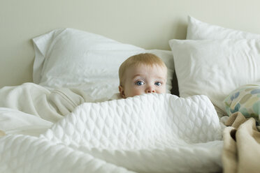 Cute baby boy hiding amidst duvet on bed at home - CAVF58106